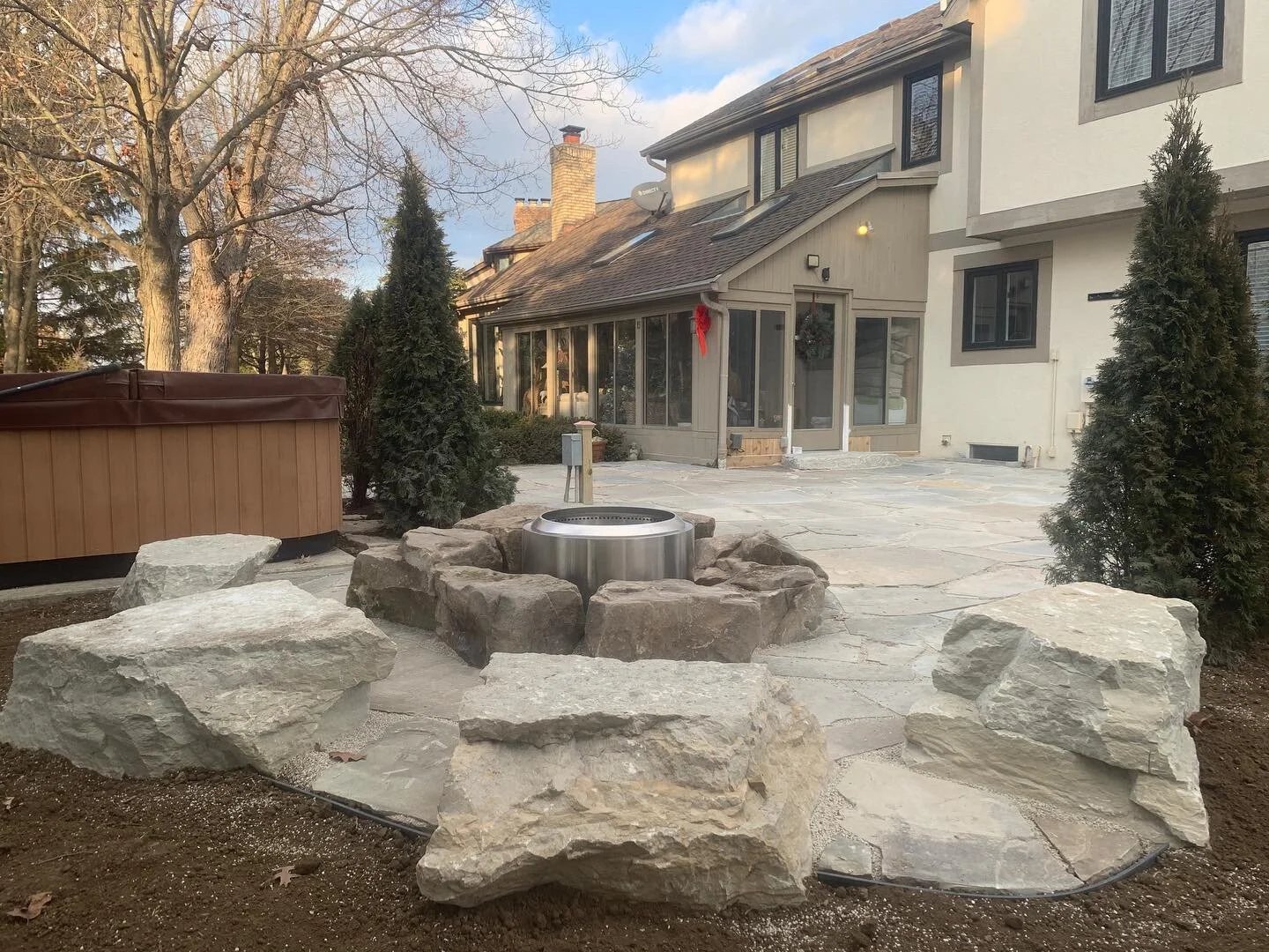 Flagstone patio with a boulder fire pit ring, hot tub, and evergreen plantings