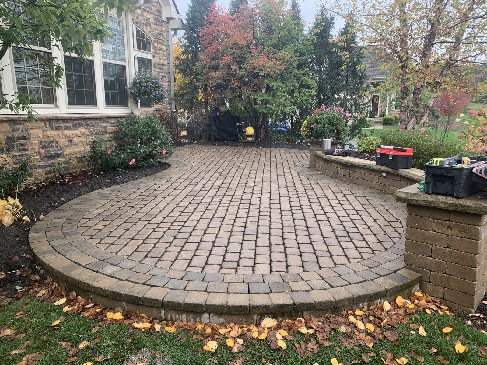 Round cobblestone paver patio with a seat wall and stone pillars